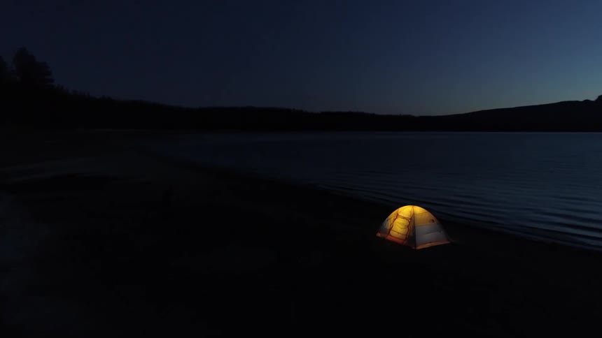 Aerial view of a tent set up next to the lake at dusk
