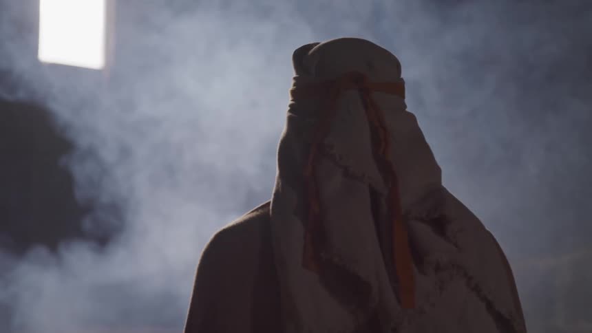 Man wearing head covering stands in foggy room looking up at window