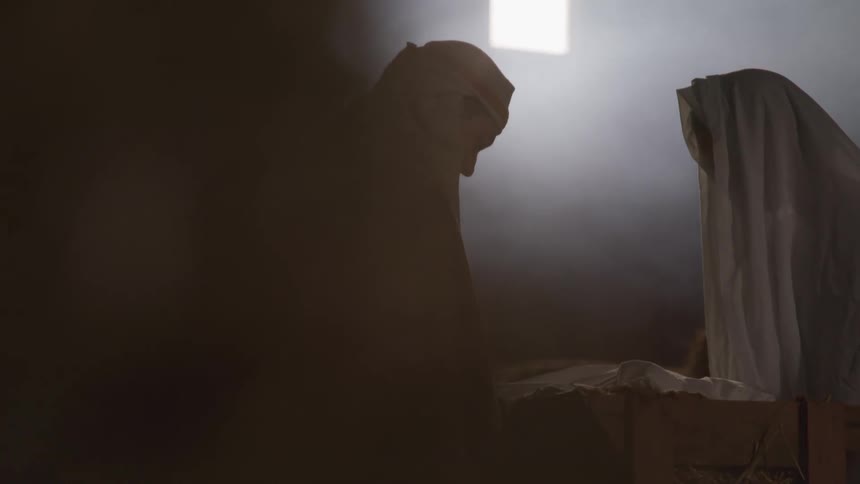 Two people in robes look down at a box