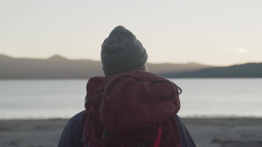 Male hiker stands and watches the lake at dusk