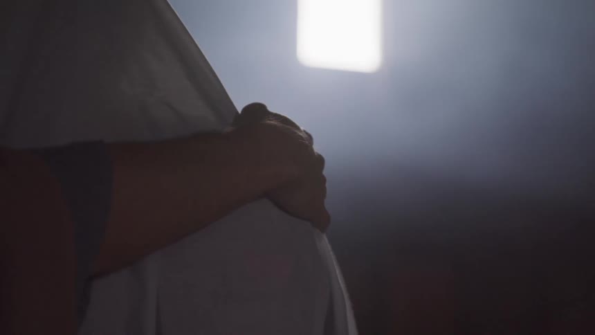 Pregnant woman standing in a dark room with her hand on her belly