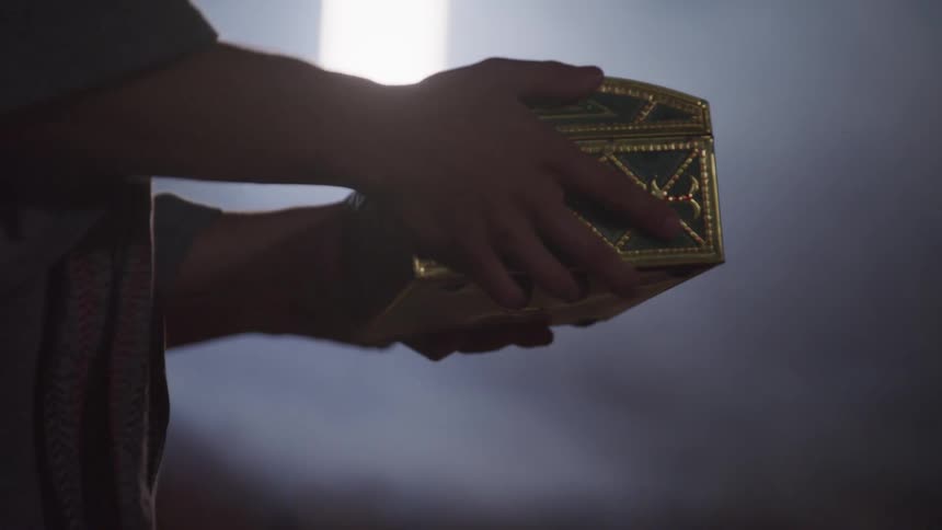 A person raises up a gold inlaid box
