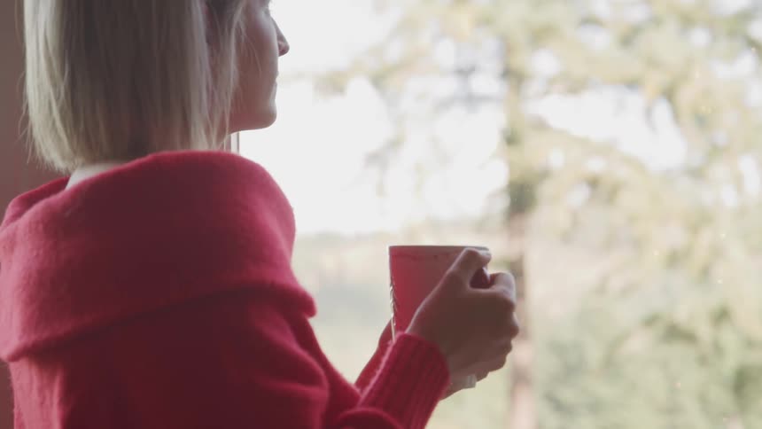 White woman holding a cup of coffee while staring at outside
