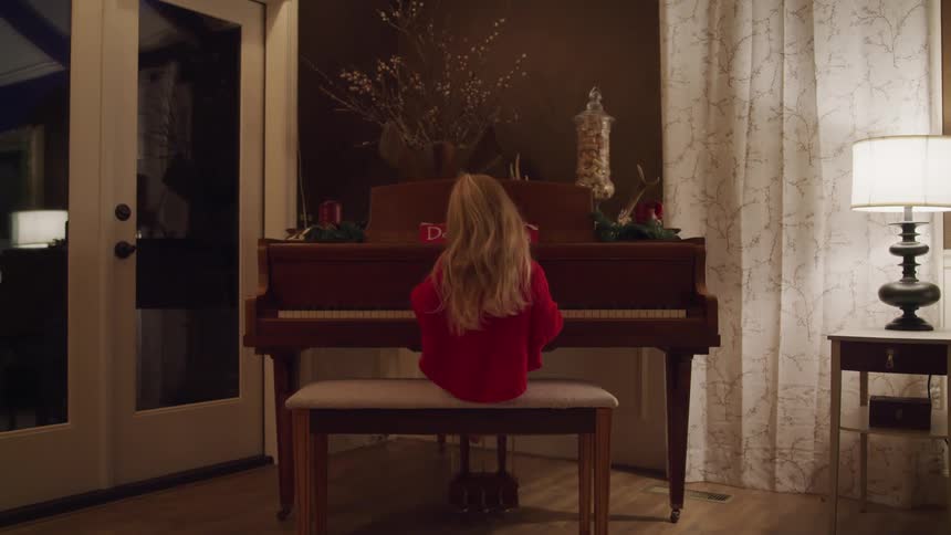 A young girl sits on a piano bench in a living room