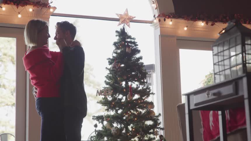 Husband and wife dance and kiss each other next to the christmas tree in the living room at home