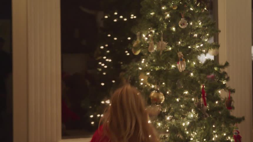 A little girl running to a christmas tree and opening a gift