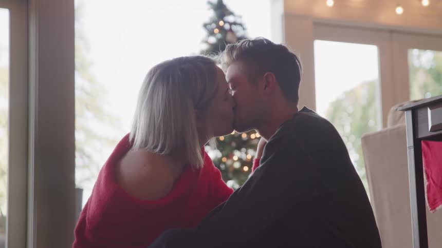 A man and woman kiss beside a christmas tree