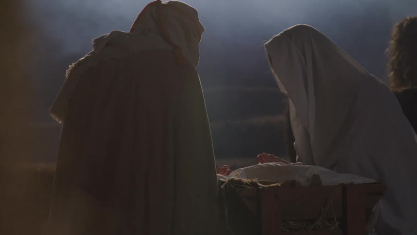 Actors portraying joseph and mary looking down at baby jesus in the manger