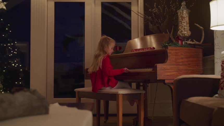 Blonde little child plays the piano near the christmas tree