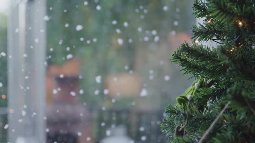 Snow slowly falling down outdoors through the window close to christmas tree