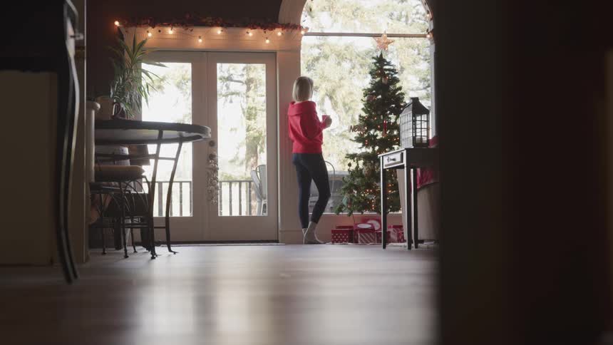 A woman walks over to the window with a drink