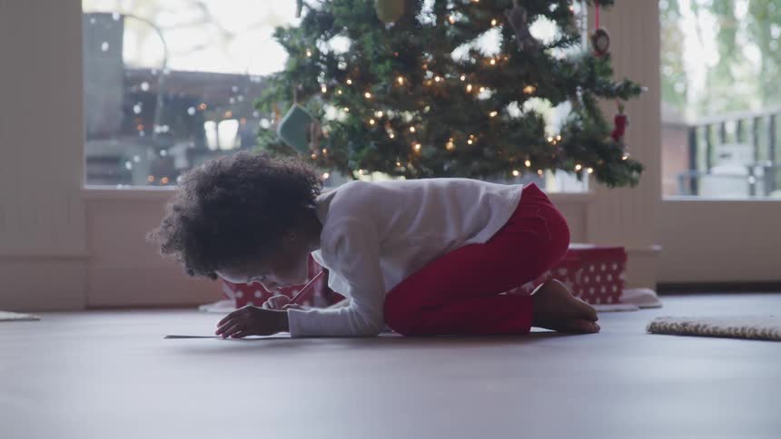 Black child writes a letter to santa next to the christmas tree