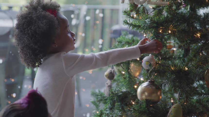 A little girl puts a decoration on a christmas tree