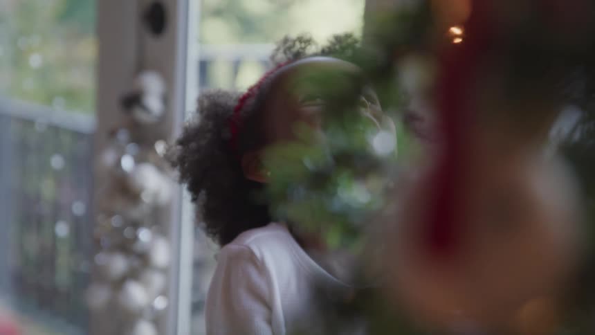 Black girl looking up to the christmas tree and happily laughing