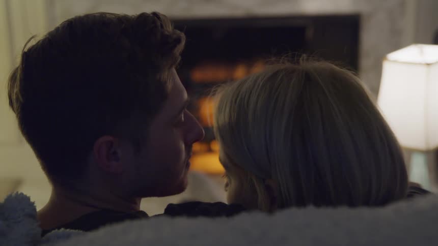 White couple romantically sitting together at the couch in front of the fireplace
