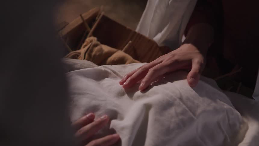 Two women have their hands over bedding in a cradle