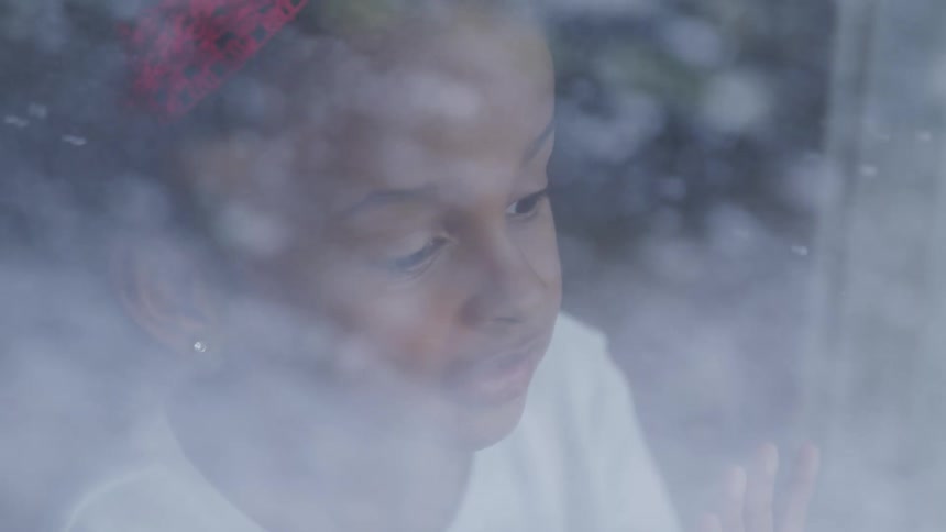 Little girl watching the snow fall from a window indoors