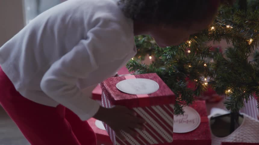A female child shaking a christmas gift under the tree