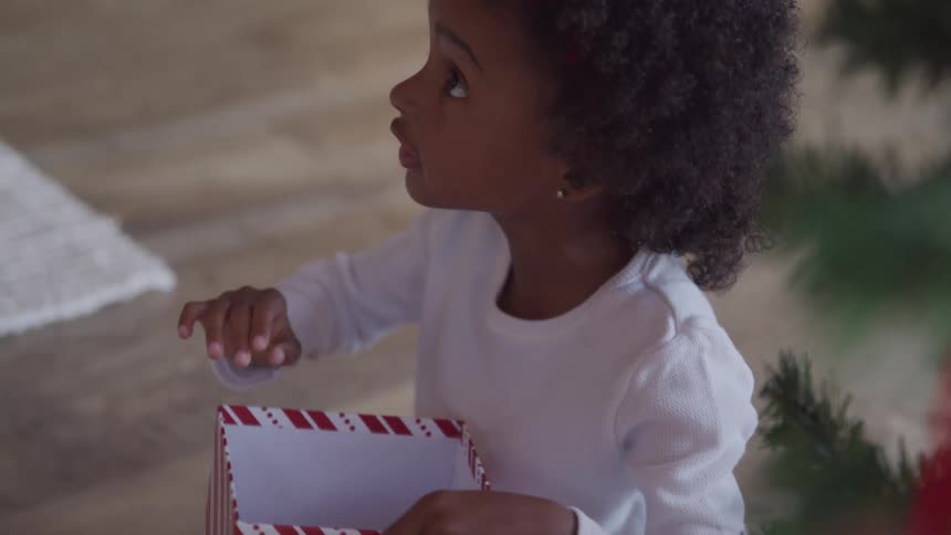 A young girl looks up from a gift box beside a christmas tree