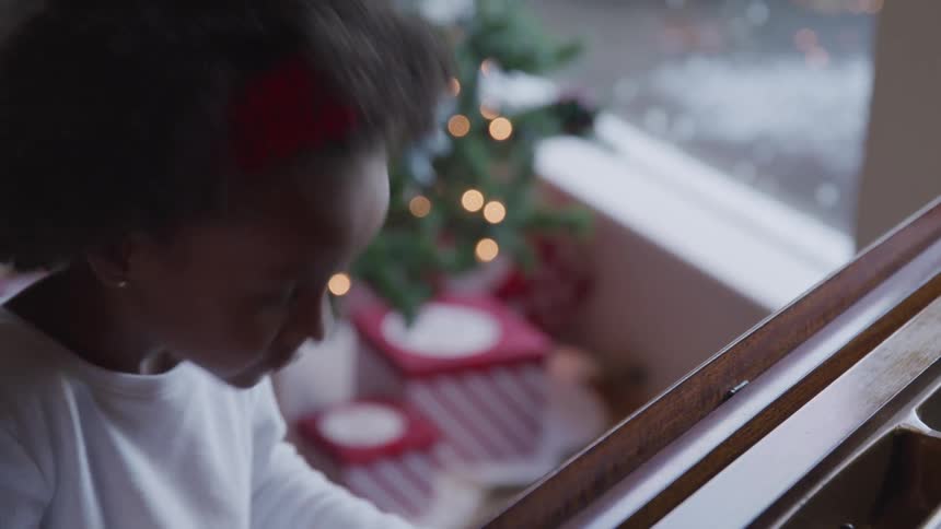 Black little girl presses the piano keys randomly near the christmas tree