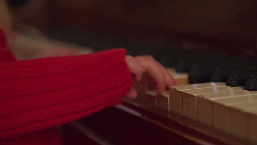 A child plays the piano in a red sweater with her little fingers and hands the only parts of her body shown