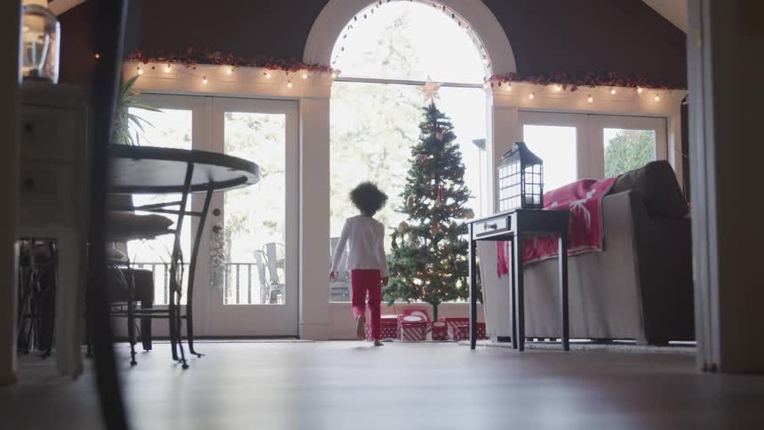 A young girl runs to her familys christmas tree and grabs a present underneath to open