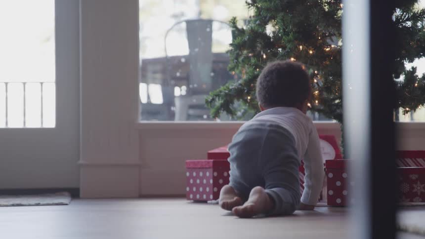 Baby crawling towards the gifts under a christmas tree