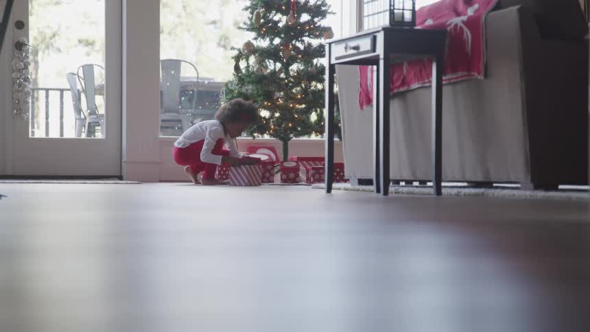 Girl picks up present from under christmas tree and gives it a experimental shake before opening it