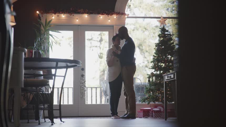 Husband and wife dance next to the christmas tree in a room