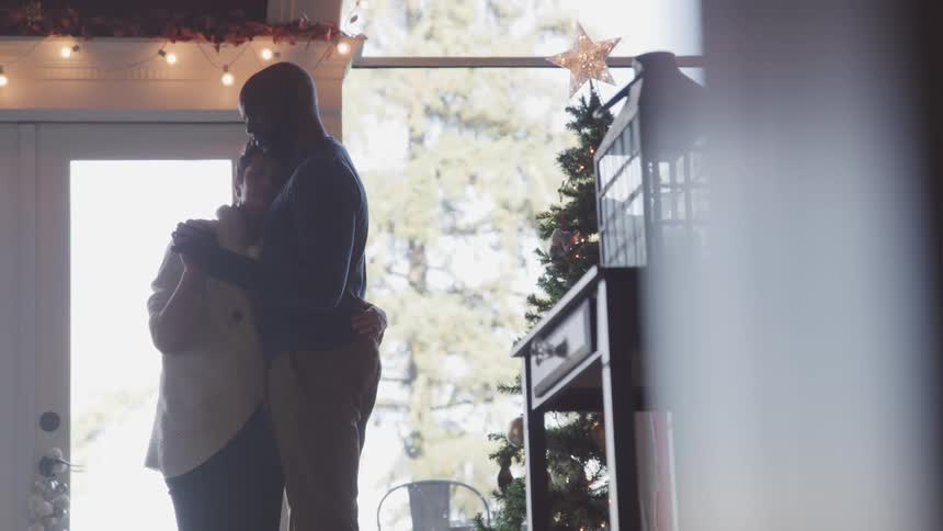 Couple romanticly slowly dancing inside a house next to a christmas tree