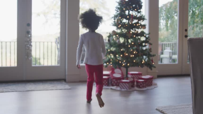 Female child running towards a christmas tree with lights shimmering and presents underneath