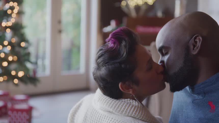 A man and woman kiss in front of a christmas tree