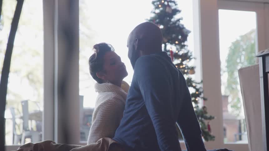 Couple kissing while sitting at floor indoors close to a christmas tree