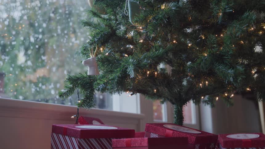 Snow falling down through the window close to the christmas tree