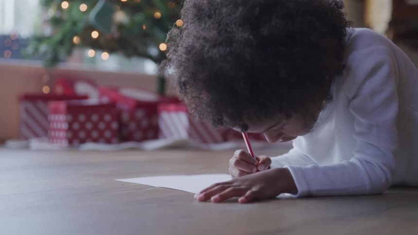 Black child writes a letter to santa next to the christmas tree