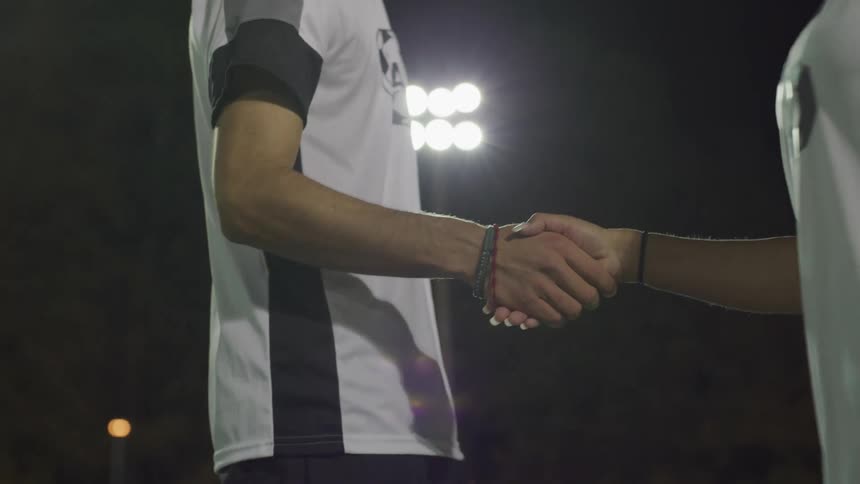 Male and female football player shake hands with each other on the football field at night
