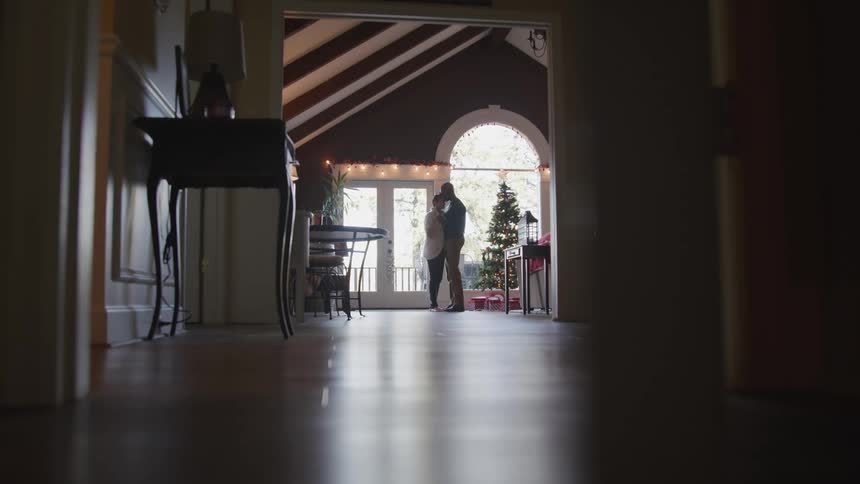 Couple slowly dancing next to the christmas tree indoors