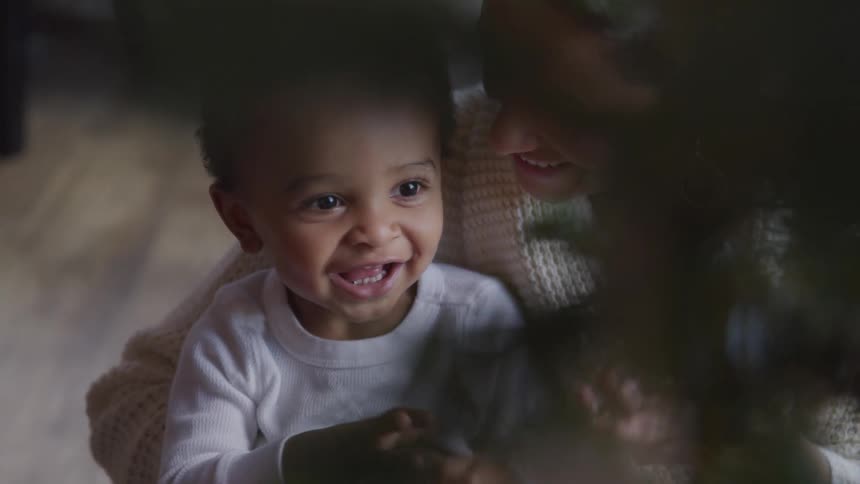 White woman playing with a black baby close to a christmas tree