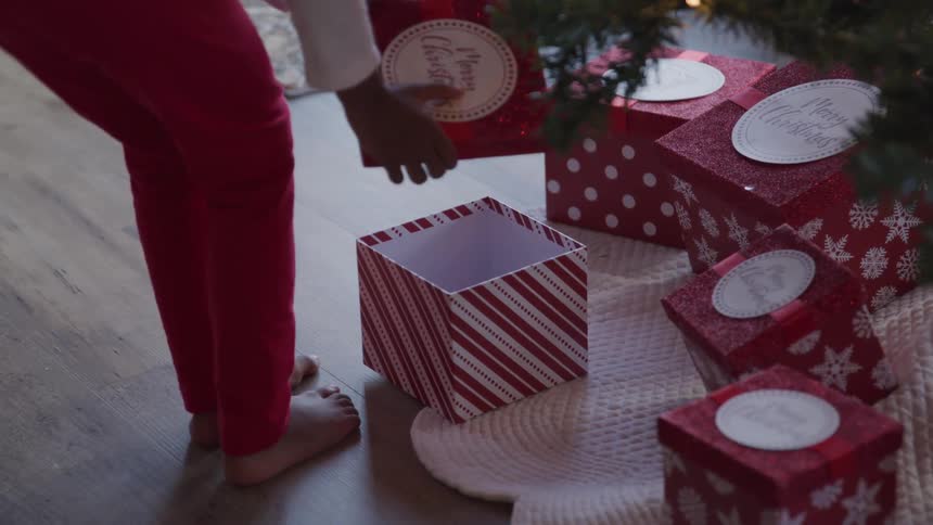 Kid opening up a gift close to the christmas tree