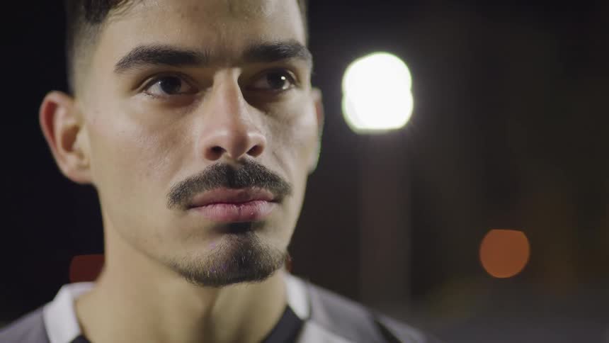 Male footballer stands and looks ahead on the football field at night
