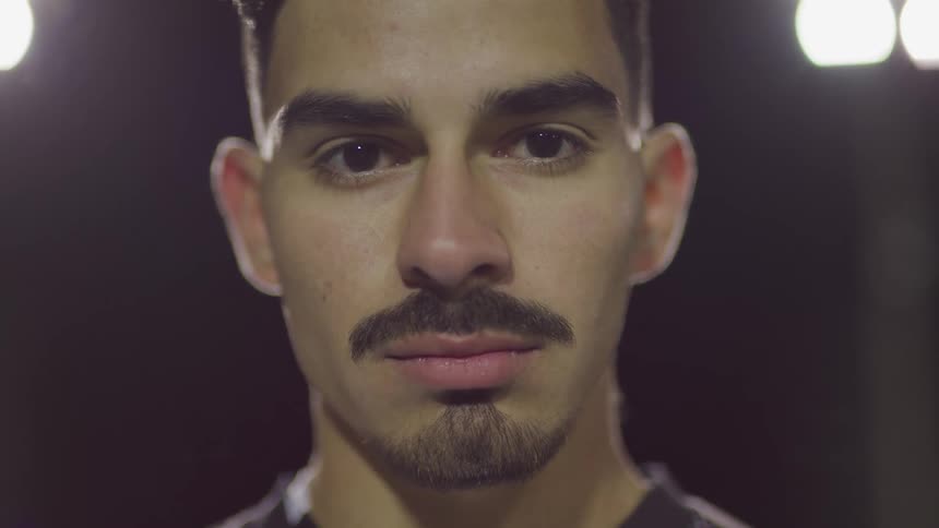 Male footballer stands and looks at the camera on the football field at night