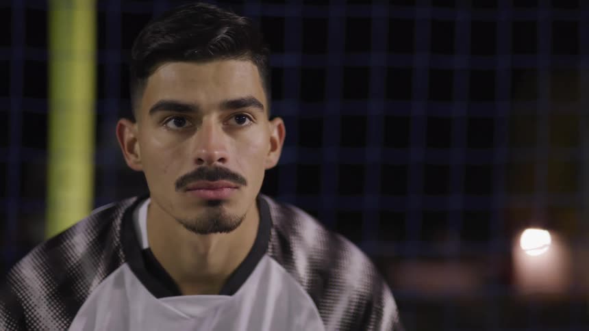 Male footballer plays football on the football field at night