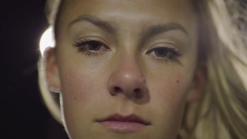 Female blonde footballer stands and looks at the camera on the football field at night