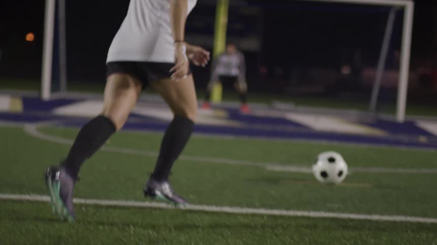 Female soccer playing taking a shot towards the goalie during a soccer game