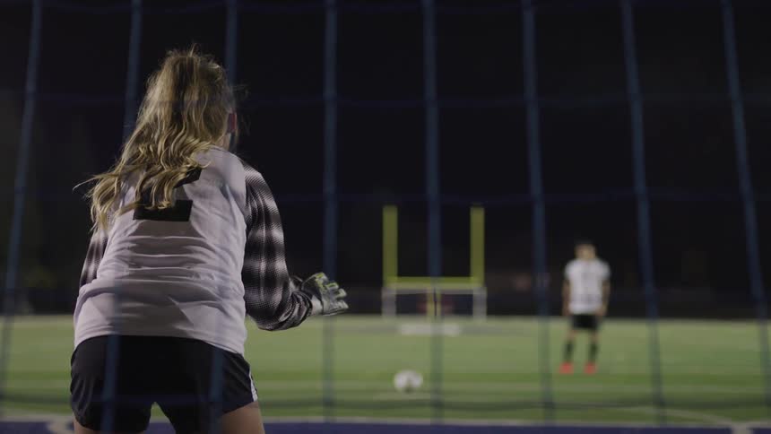 A woman stands in front of a soccer goal waiting for the opponent to kick the ball