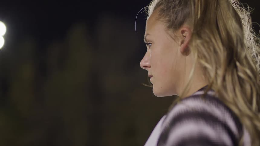 Female footballer stands and looks ahead on the football field at night