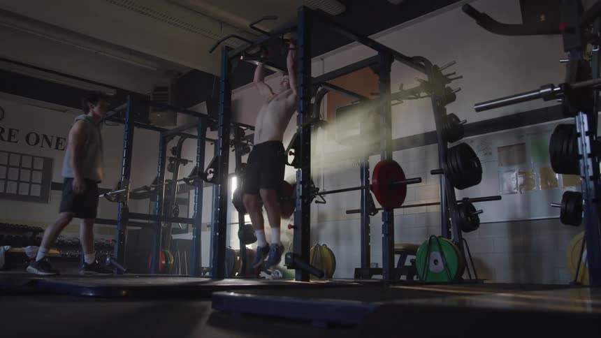 Shirtless sweaty man pulls up in the gym