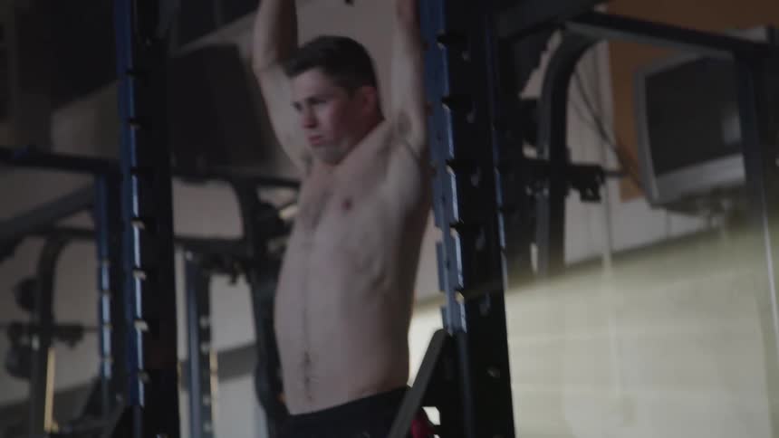 Shirtless man pulls up in the gym
