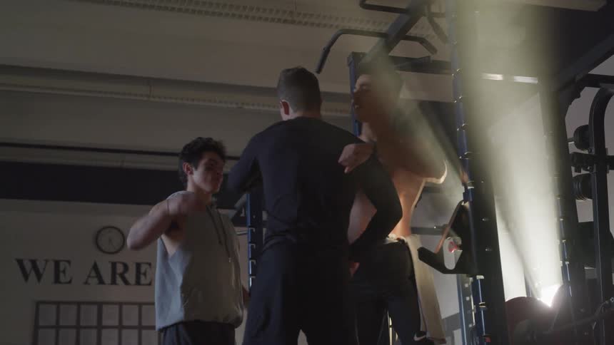 Three males high five and shake hands inside a fitness gym