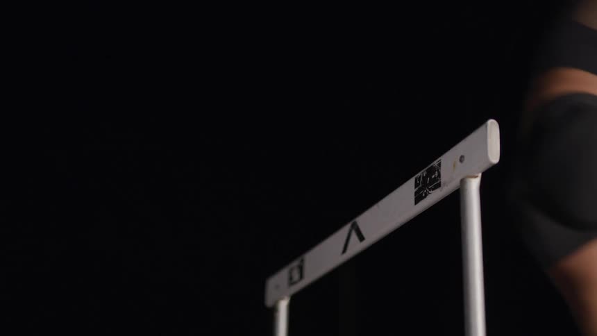 Female athlete jumps over a hurdle on the dark background